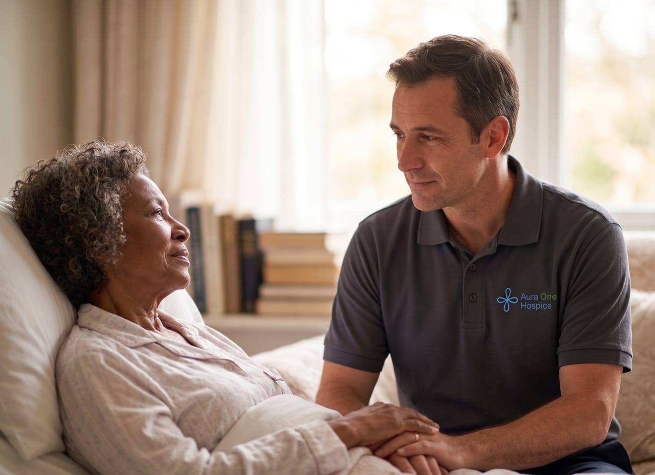 An Aura One Hospice caregiver sitting with and holding the hand of an elderly woman resting at home